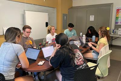 A group of PLTL students and a Peer Leader sit around a table discussing answers to a workshop packet.